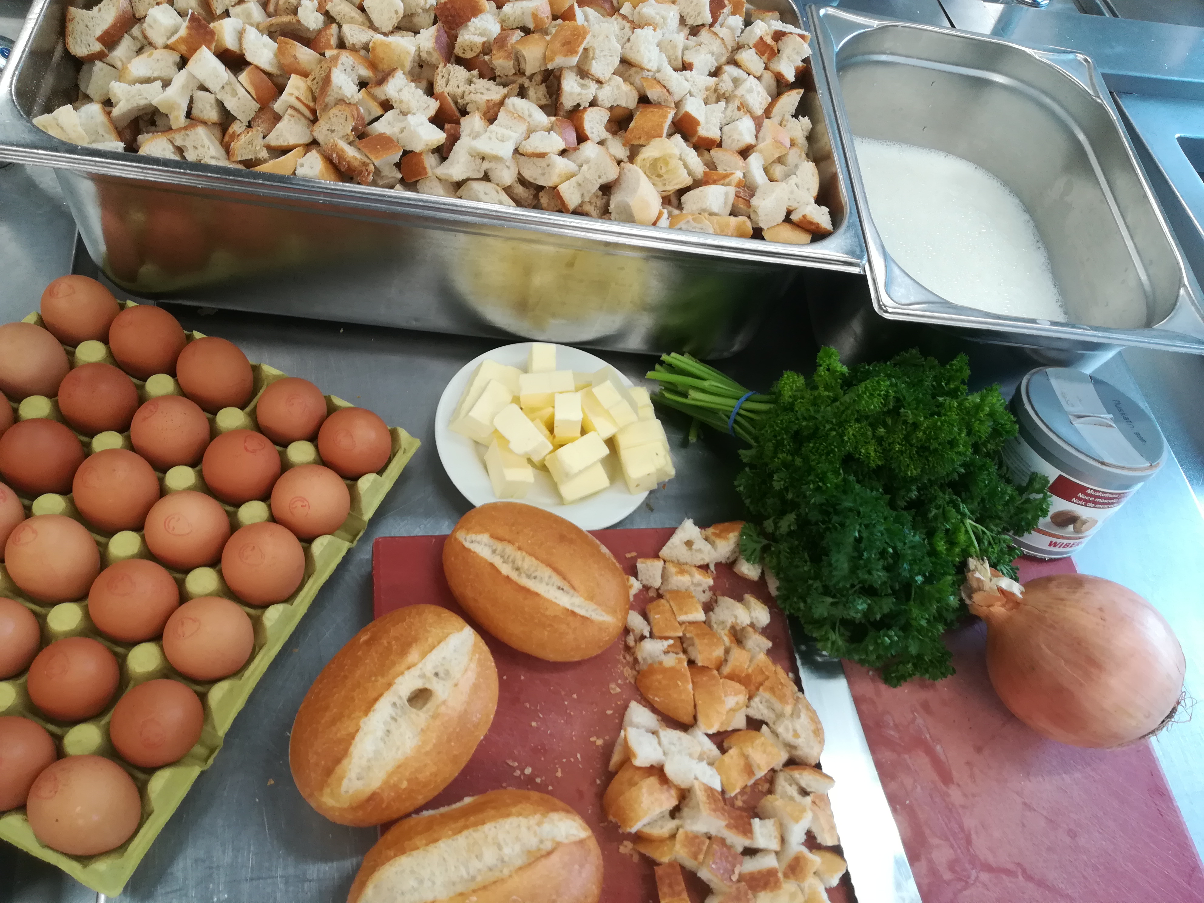 Zutaten Semmelknödel Brotstückchen, Semmeln, Zwiebeln, Butter, Eier und Petersilie liegen bereit zur Verarbeitung auf einem roten Brett