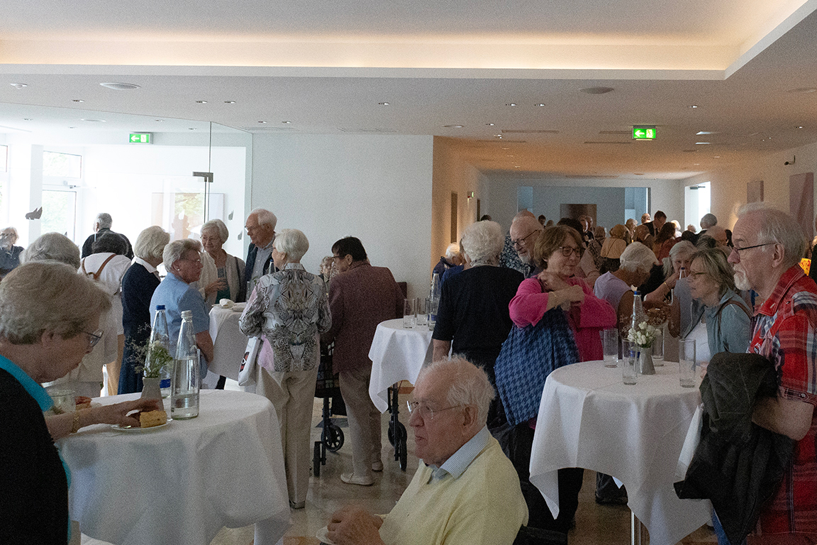 Die Besucher*innen der Gesundheitssprechstunde stehen an kleinen Tischen, unterhalten sich und essen etwas