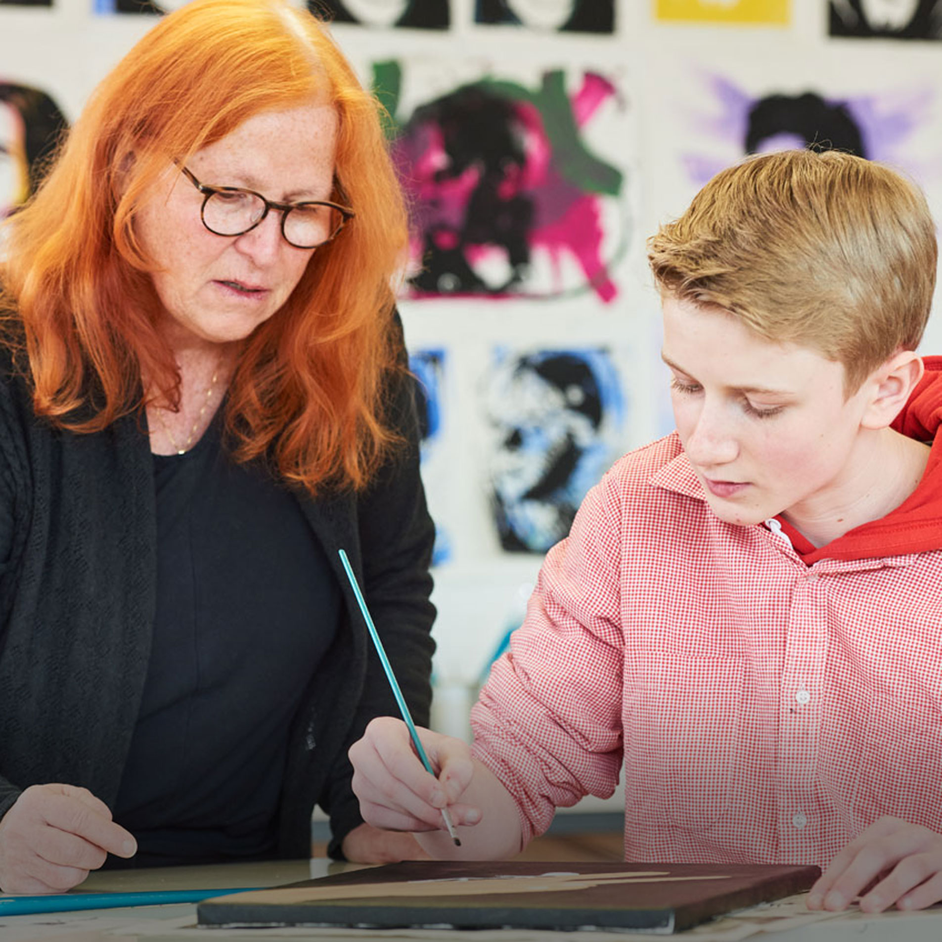 Eine Lehrerin schaut einem Schüler beim Malen im Kunstunterricht zu