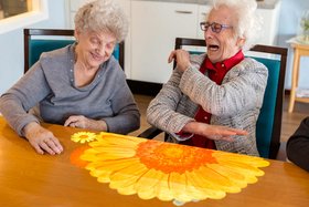 Augustinum Sanatorium Schwindegg Tovertafel Zwei Seniorinnen sitzen an einem Tisch, auf den mithilfe einer Tovertafel eine Blume projiziert wurde