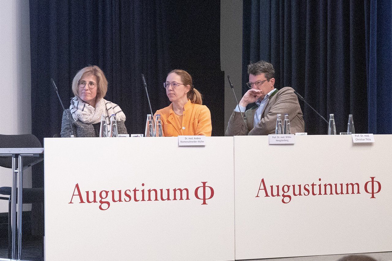 Augustinum Klinik Symposium Vorsitz Der Vorsitz des ersten Symposiums - bestehend aus zwei Frauen und einem Mann - sitzt auf der Bühne