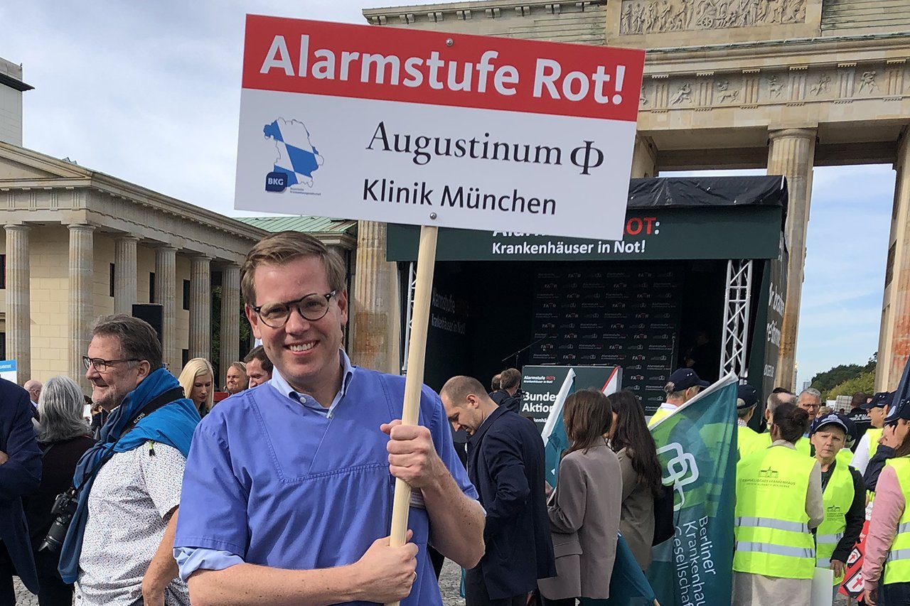 Augustinum Klinik Aktionstag Ein Mitarbeiter der Augustinum Klinik hält ein Schild mit der Aufschrift "Alarmstufe Rot! Augustinum Klinik München"
