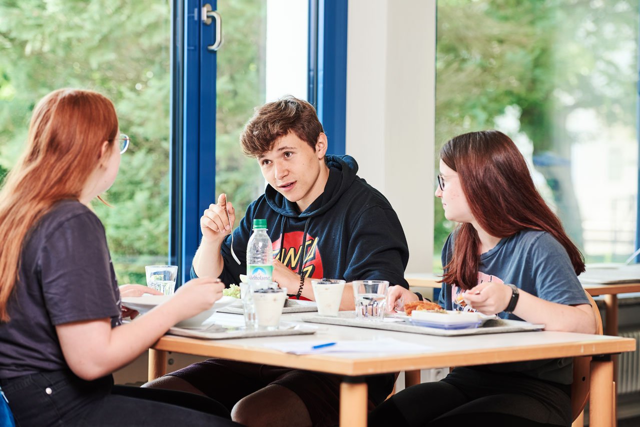 Mensa Schüler*innen sitzen an einem Tisch in der Mensa