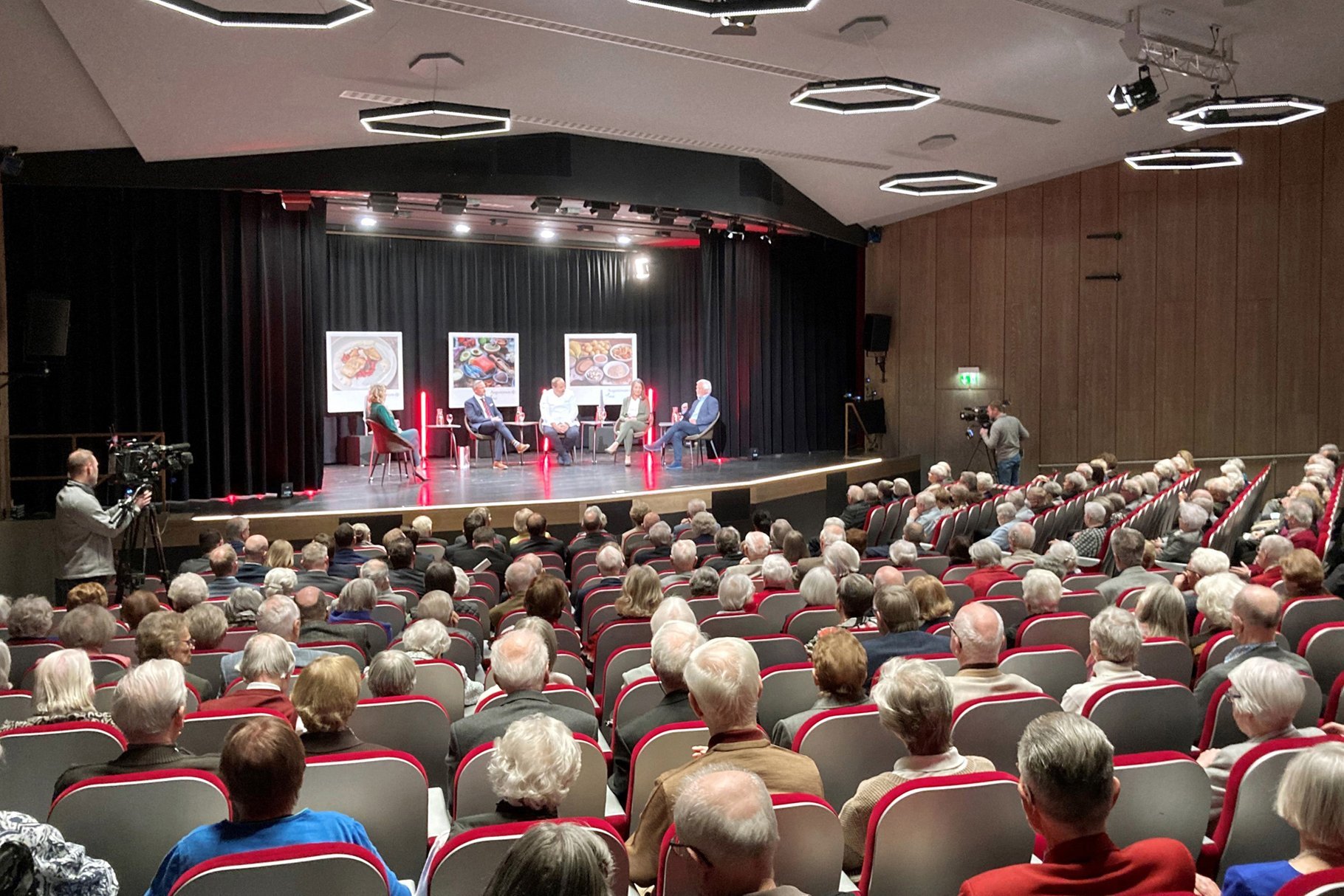 Theatersaal im Augustinum Stuttgart-Sillenbuch Senior*innen sitzen im Theatersaal während sich fünf Leute auf der Bühne unterhalten