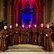 Magic Gregorian Night Acht Personen in braunen Ordensgewändern stehen vor dem Altarraum einer Kirche mit farbig beleuchteten Spitzbogenfenstern und Kreuz im Hintergrund