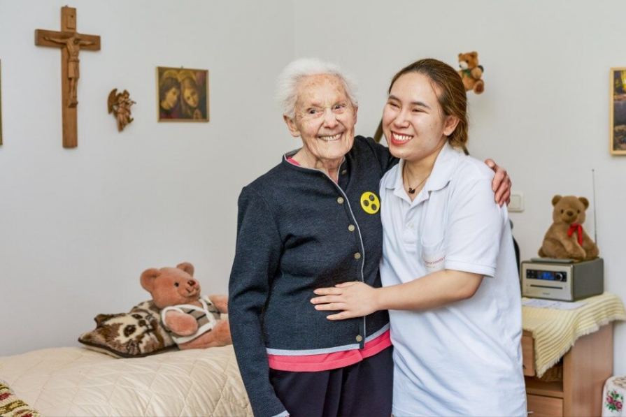 Eine Seniorin und eine Mitarbeiterin umarmen sich und lächeln 