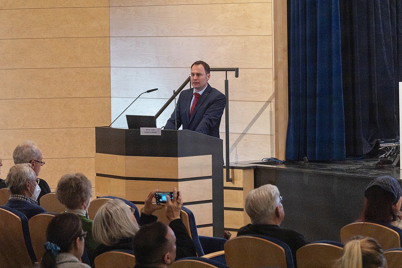 Augustinum Klinik Symposium Dr. Patzelt Dr. Patzelt von der Augustinum Klinik steht an einem Rednerpult vor dem Publikum während er seinen Vortrag hält