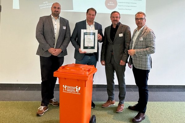 Die drei Projektbeteiligten des Augustinum zusammen mit dem Geschäftsführer von United against Waste halten die Urkunde für die Auszeichnungen in den Händen, im Vordergrund eine orangene Mülltonne