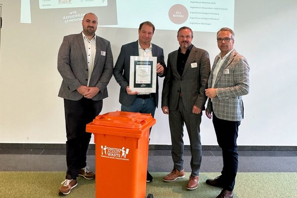 Auszeichnung Lebensmittelmüll UAW 2023 Die drei Projektbeteiligten des Augustinum zusammen mit dem Geschäftsführer von United against Waste halten die Urkunde für die Auszeichnungen in den Händen, im Vordergrund eine orangene Mülltonne