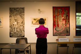 Eine Frau hat den Rücken zur Kamera gewendet und betrachtet Kunstwerke, die an einer Wand hängen