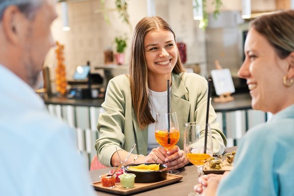 Treffen im Vierundsiebzig Drei Gäste sitzen an einem Tisch im Vierundsiebzig, unterhalten sich, lachen und trinken einen Spritz