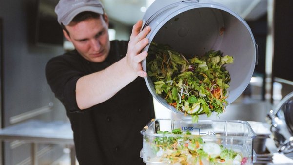 Ein Mitarbeiter wirft Salat aus einem großen Eimer zum Wiegen in die Abfalltonne