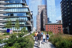 Mehr als Wolkenkratzer Menschen spazieren auf einem begrünten Fußweg zwischen modernen Hochhäusern und historischen Backsteingebäuden in im dicht bebauten New York.