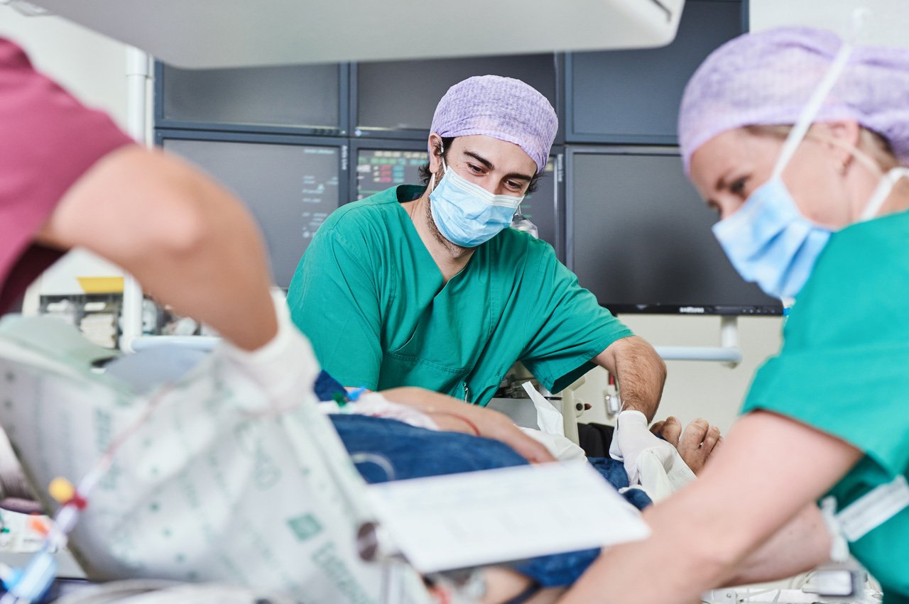 Zusammenarbeit von Ärzten und Pflege Zwei Pflegekräfte versorgen einen Patienten nach einem kardiologischen Eingriff