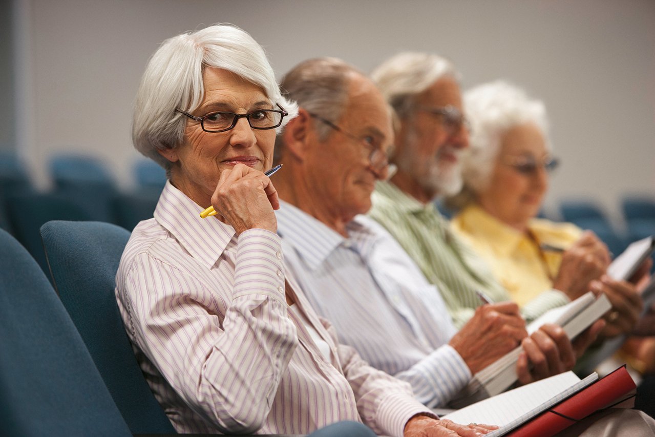 Sprachkurs Vier Senior*innen sitzen mit Stift und Papier in einem Saal
