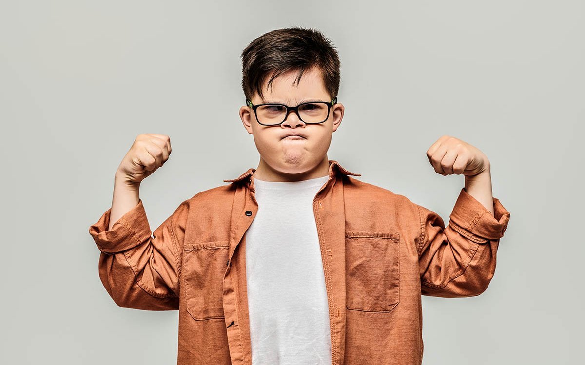 Kleiner Junge zeigt mit grimmigem Gesicht seine Muskeln