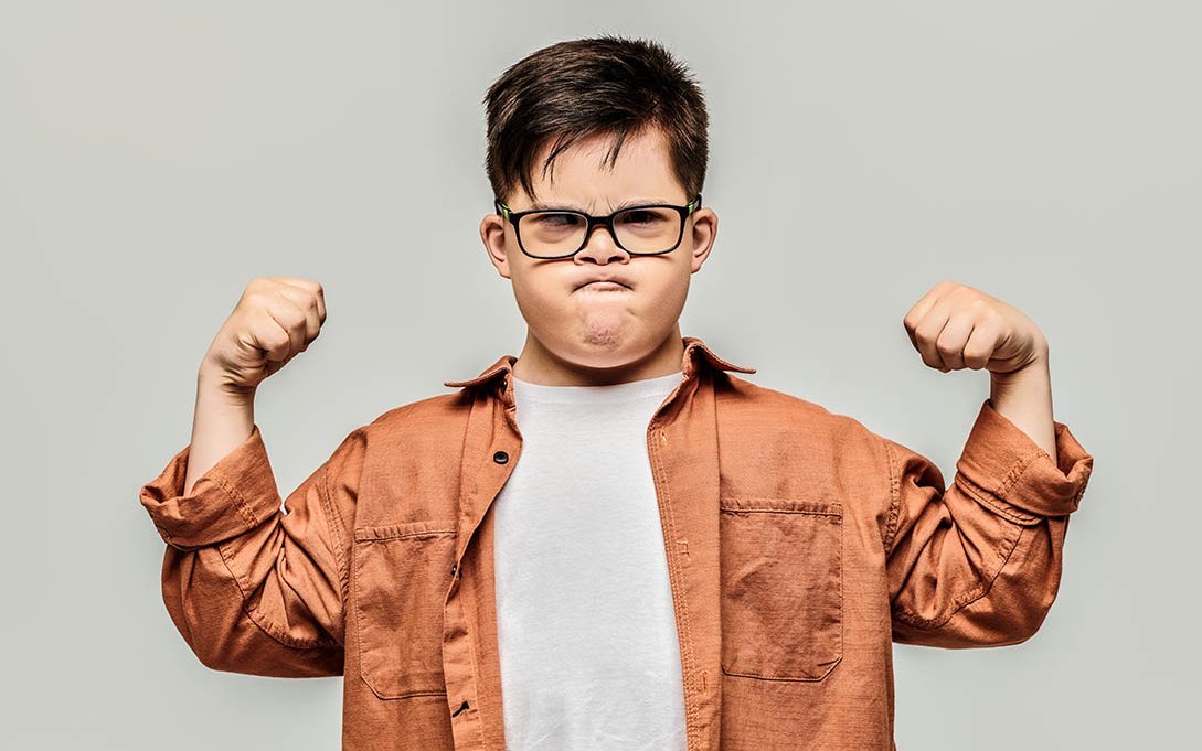 Kleiner Junge zeigt mit grimmigem Gesicht seine Muskeln