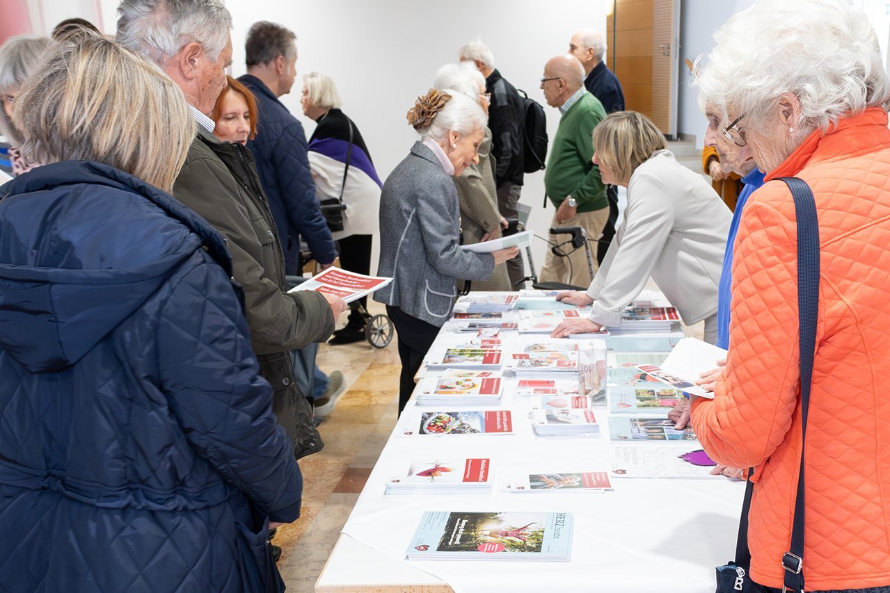 Augustinum Klinik Herzwochen Herzstiftung Besucher*innen der Veranstaltung lesen Broschüren und informieren sich an einem Stand der Deutschen Herzstiftung