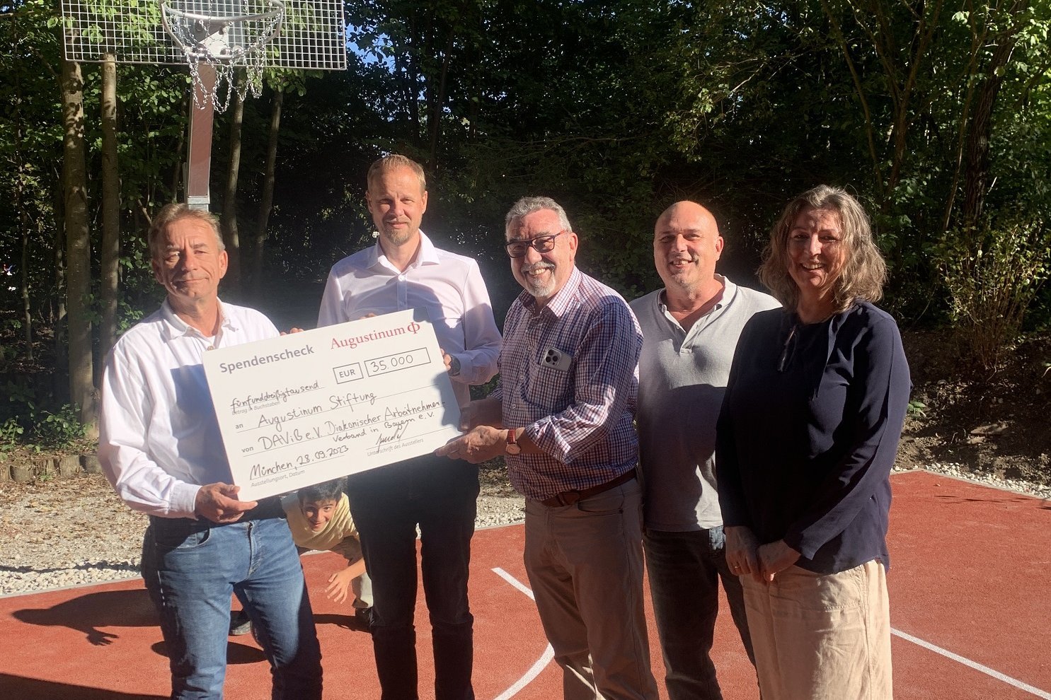 Ein Gruppenbild auf dem Basketballplatz des Augustinum Studienheims, bei dem der Spendenscheck empfangen wird 