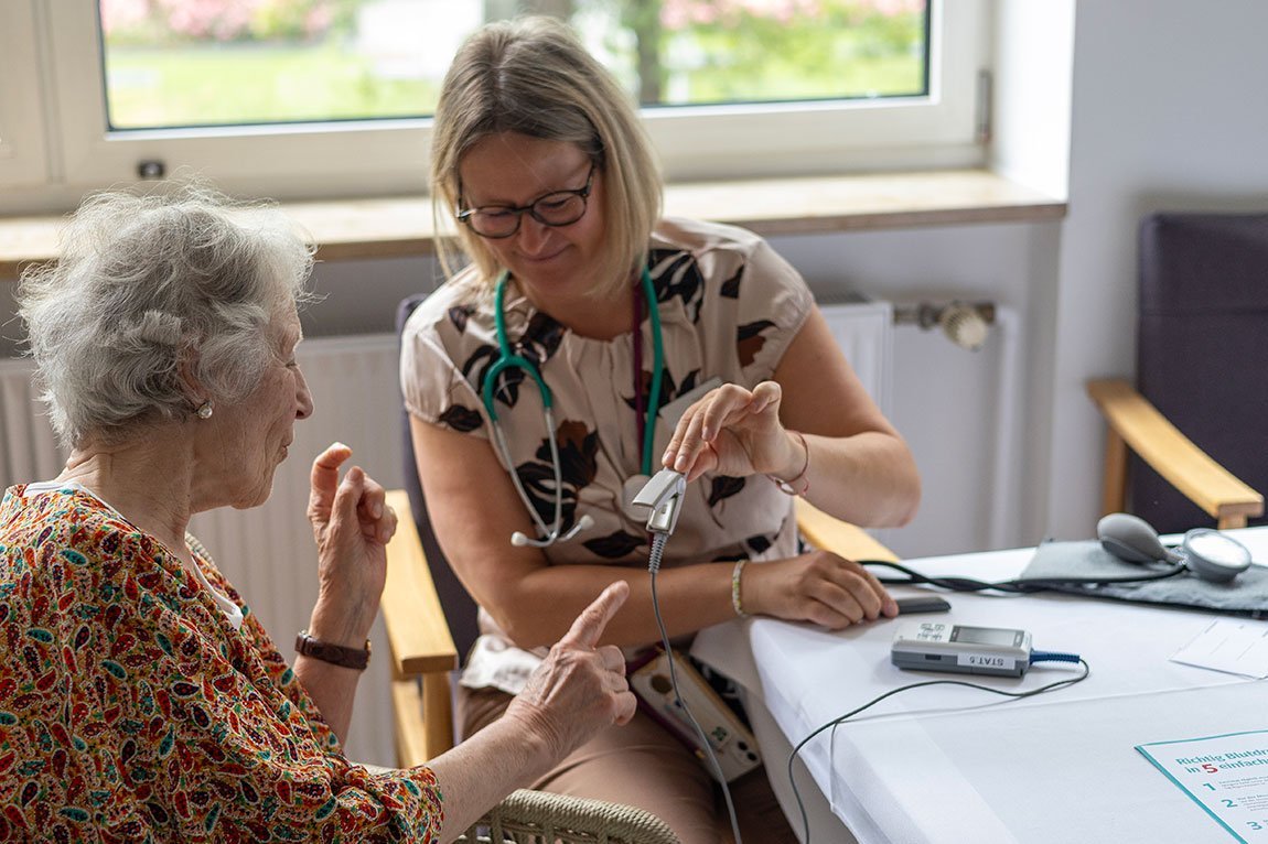 Eine Mitarbeiterin der Augustinum Klinik misst den Sauerstoffgehalt des Blutes einer Seniorin 