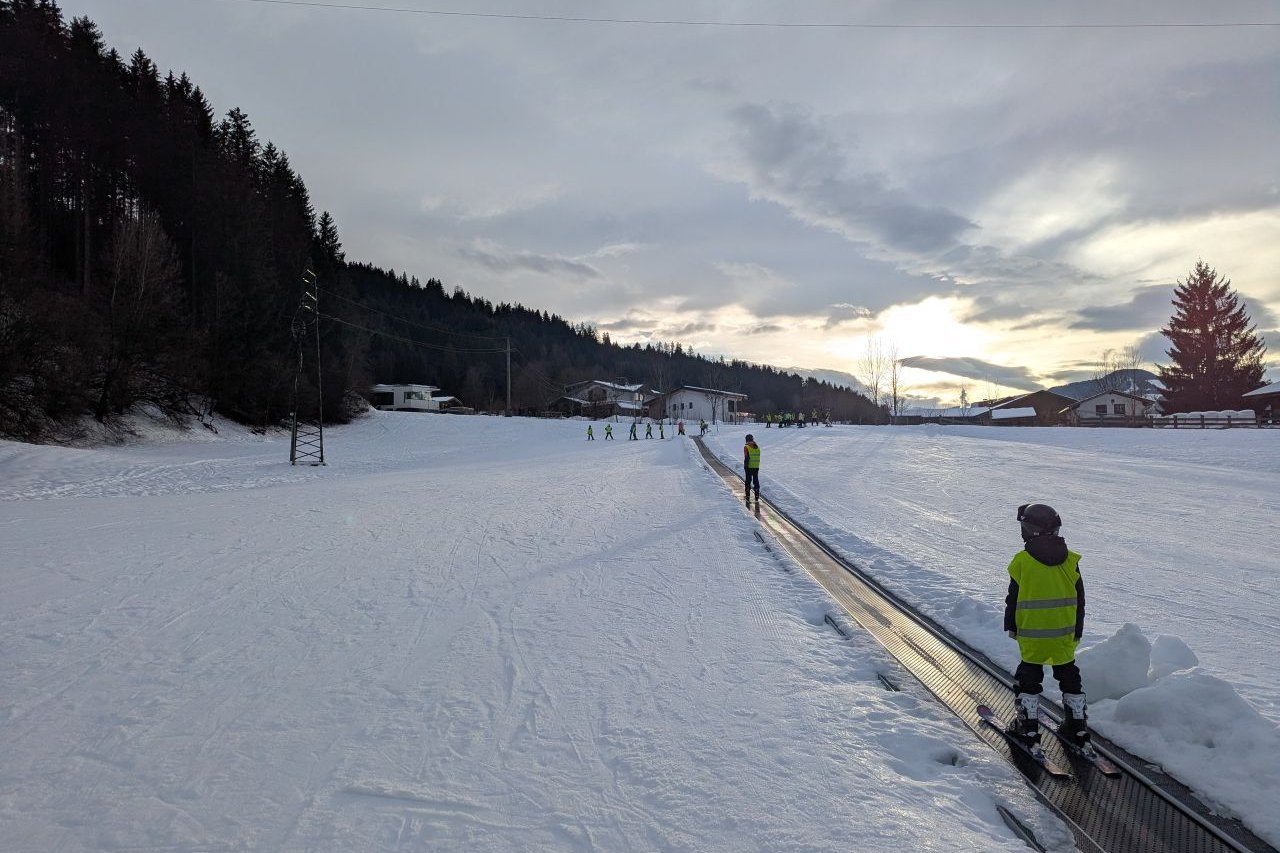 Augustinum Samuel-Heinicke-Realschule Wintersportwoche Eine große Schneefläche, durch die ein Weg führt, auf dem sich die Schüler*innen auf Skiern befinden