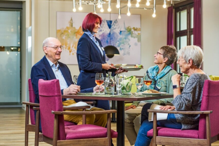 Drei Senior*innen erhalten ihr Essen von einer Mitarbeiterin des Restaurants