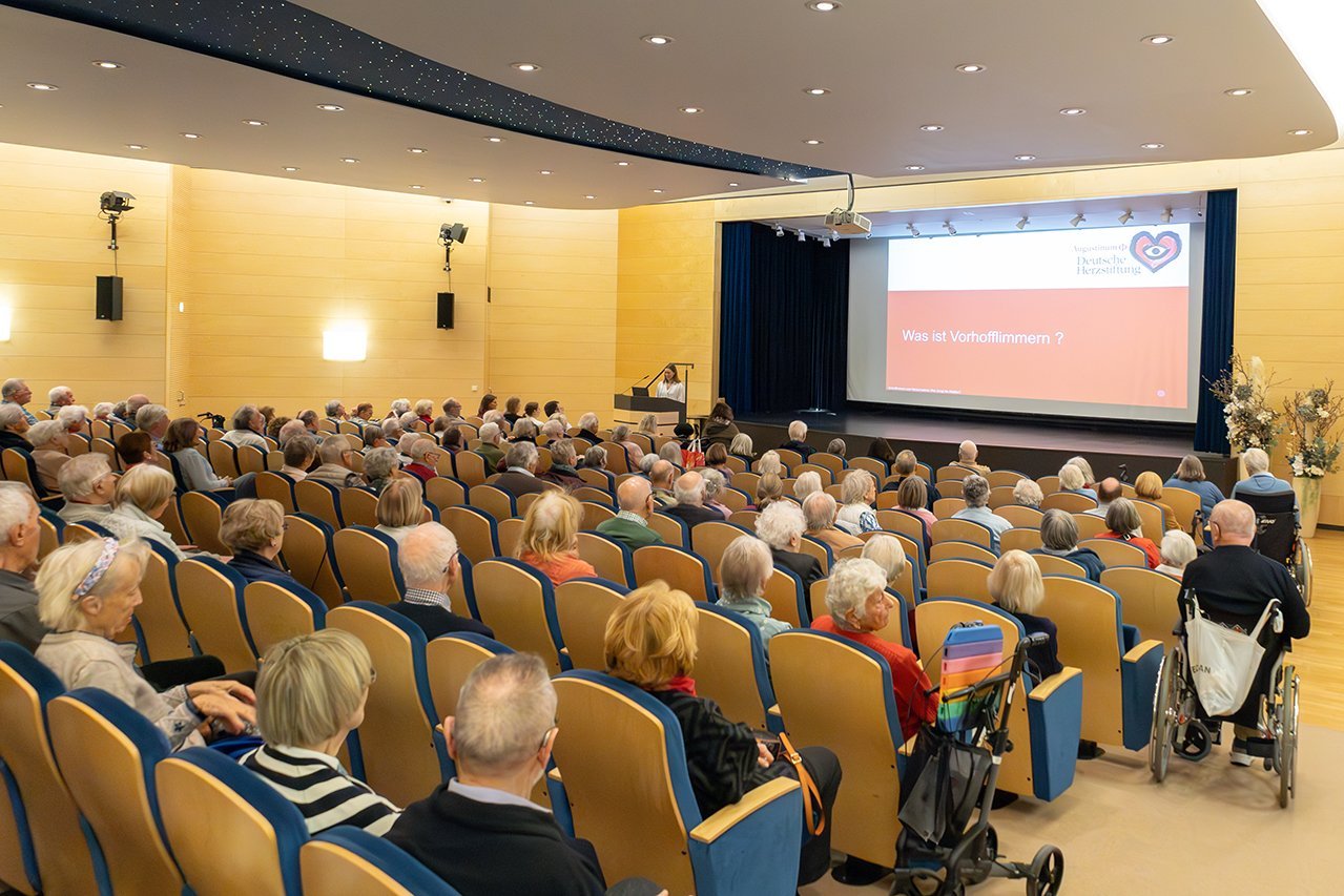 Augustinum Klinik Herzwochen Thomas Viele Senior*innen sitzen in einem Theatersaal während eine Dozentin vor der Bühne einen Vortrag hält