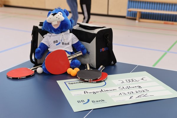 Augustinum Spende Tischtennis Der Spendenscheck, Tischtennisschläger und ein Kuscheltier der BBBank auf einer Tischtennisplatte