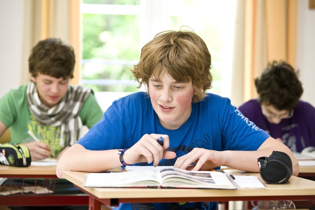 Ein Junge sitzt im Unterricht und vor ihm liegen ein Heft und ein Schulbuch