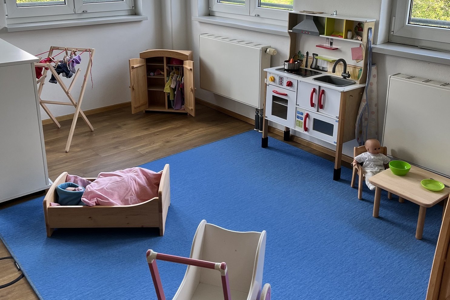 Man sieht eine Puppenspielecke mit Kinderwagen, Einkaufsladen und anderen Gegenständen
