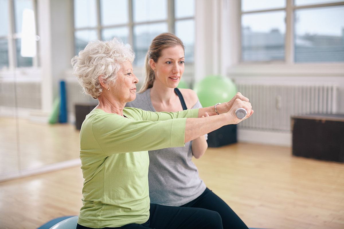 Sitzgymnastik Eine Trainerin hilft einer Seniorin bei einer Gymnastik-Übung